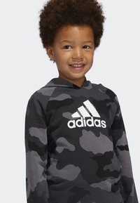Felpa con cappuccio in un motivo camouflage nero e grigio. Presenta un logo Adidas bianco in evidenza sulla parte anteriore. Tessuto morbido, maniche lunghe.