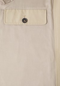 Chemise beige à boutons avec une poche poitrine dotée d'un bouton noir, texture de tissu lisse et lignes nettes le long des bords.