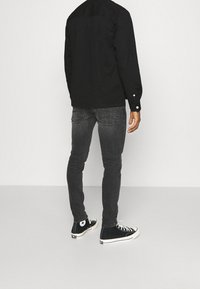 Camisa negra de manga larga sobre jeans ajustados grises y zapatillas altas negras. Los jeans tienen un ligero desgaste y bolsillos traseros con costuras.