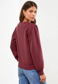 Vinski pulover s pufastimi rokavi, rebrastimi manšeti in robom. Mehka tekstura; ima okrogel izrez in sproščen kroj.