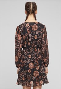 Rochie neagră cu mânecă lungă, cu o textură transparentă, brodată cu chenaruri aurii și desene circulare, având un talie elastică și un tiv învolburat.