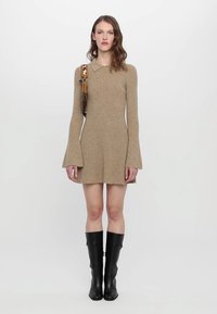 Rochie tricotată bej cu guler, cu mâneci clopot; model purtând cizme negre până la genunchi, cu un accesoriu cu curea cu model.