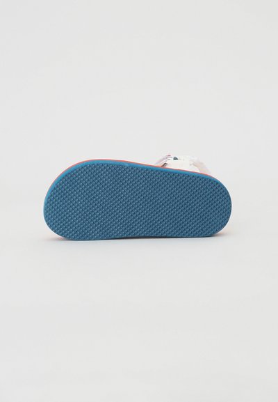 Zapatilla con suela de goma azul que presenta un patrón texturizado, parte superior blanca y un diseño colorido en la correa cerca de la suela.