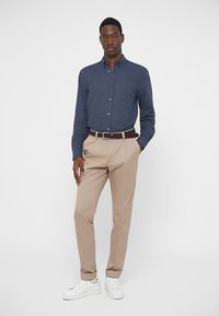 Camisa azul-marinho com botões, calças bege, cinto trançado castanho e tênis brancos. Tecido suave com um corte ajustado e uma textura subtil.