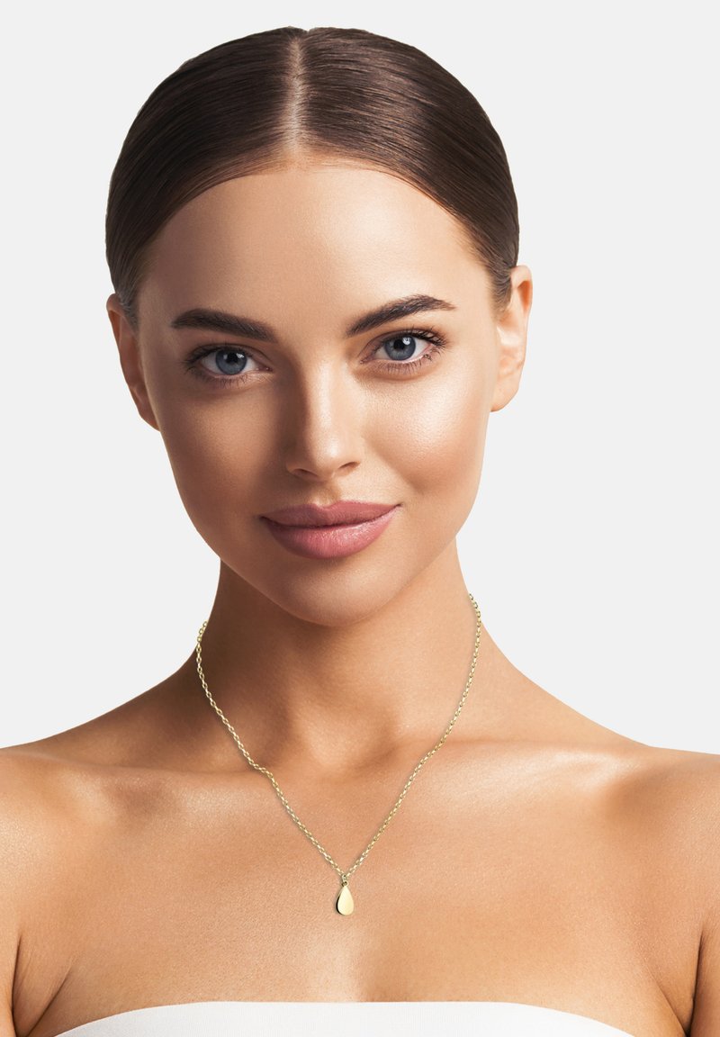 Guldpläterat halsband med en delikat kedja och en droppformad berlock, som vilar på bara axlar mot en neutral bakgrund.