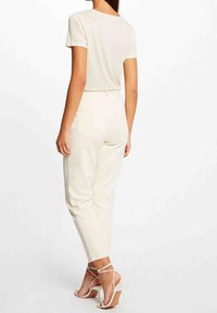 T-shirt attillata color crema con maniche corte, abbinata a pantaloni crema a vita alta con tasche sul retro e tacchi bianchi con cinturino alla caviglia.