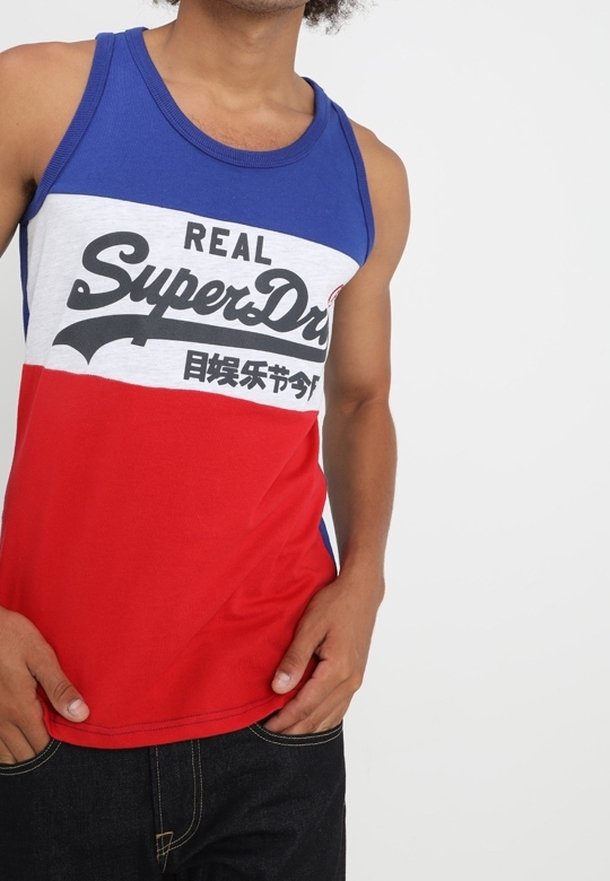 Camiseta sin mangas roja, blanca y azul con un logo gráfico "REAL SuperDry" en la parte frontal, hecha de un material similar al algodón.