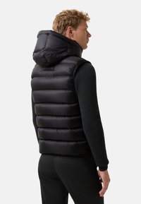 Czarna kamizelka puchowa z kapturem, z poziomymi szwami, błyszczącą teksturą i dopasowanym krojem, noszona na ciemnym swetrze.