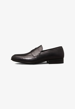 Schwarzer Herren-Loafer aus Leder mit niedrigem Absatz und Calvin Klein-Logo auf dem Riemen, von der Außenseite auf weißem Hintergrund gezeigt.