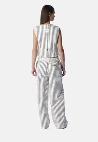 Top senza maniche tagliato e pantaloni a gamba larga bianchi con strisce verticali nere. Presenta una vita regolabile e un dettaglio con il logo sui pantaloni.