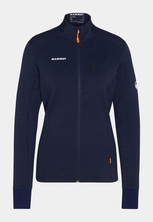 Marineblå fleecejakke med høj krave, lodrette lynlås-lommer og kontrasterende orange lynlås træk. Ribbet struktur hele vejen igennem.