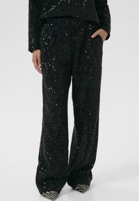 Černé kalhoty s designem ze sequinu a širokým střihem. Hladká textura a elastický pas. Doplněné o lodičky se zebřími pruhy.