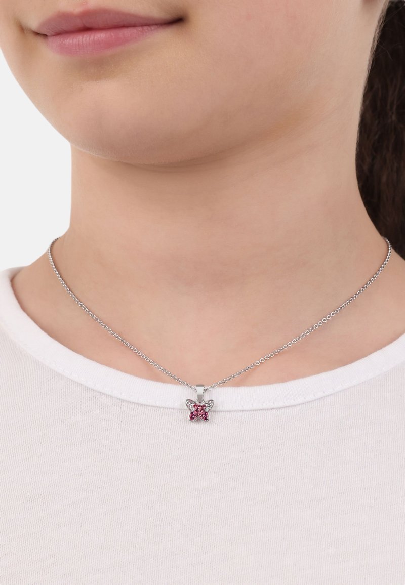 Zilveren ketting met een vlinderhanger, versierd met roze en heldere edelstenen, liggend op een wit shirt met ronde hals.