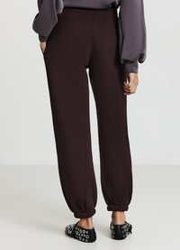 Pantalons jogger bourgogne foncé avec des poignets élastiques aux chevilles, fabriqués à partir d'un tissu lisse. Marié avec des ballerines noires aux accents argentés.