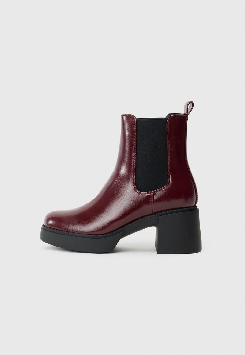 Bottine Chelsea en cuir bordeaux avec panneau latéral élastique noir, languette, talon bloc noir épais et semelle.