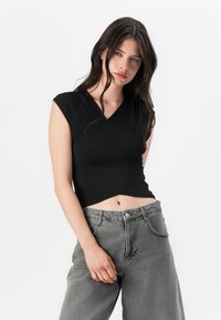 Črna, oprijeta obleka z ovitkom in V-izrezom ter kratkimi kapicami, v kombinaciji z visokim pasom sivi denim hlačami. Gladek material, minimalističen dizajn.
