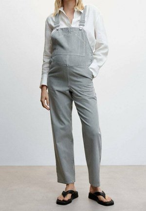 Gestreepte overalls in zwart en wit met wijde pijpen en verstelbare bandjes, gecombineerd met een wit overhemd met knopen en zwarte sandalen.