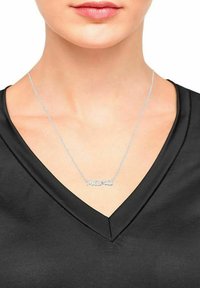 Collana d'argento con la scritta "mama" in corsivo, indossata su un top nero a V, che mette in risalto il design elegante e la delicata catena.