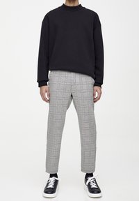 Czarny sweter z okrągłym dekoltem, szare spodnie w kratę z wąskimi paskami, czarno-białe sportowe buty, widoczne mankiety. Minimalistyczny design, luźny krój.