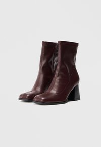 Bottines en cuir bourgogne avec un bout rond, fermeture éclair à l'avant et un talon bloc noir texturé. Surface lisse avec des détails de couture.