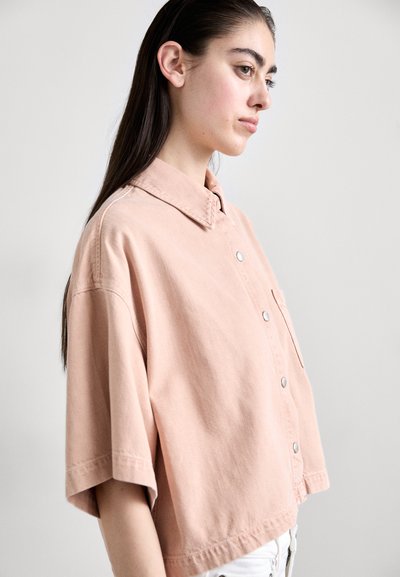 Trumpas rankovės, apykaklės marškiniai iš švelnaus persikų audinio. Yra priekiniai mygtukai, krūtinės kišenė ir laisvas kirpimas su susuktomis rankovėmis.