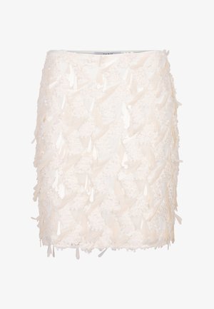 Korte A-lijn rok in crème met een gelaagde textuur, versierd met bloemen- en driehoekige appliqués, en subtiele reflecterende accenten doorheen.