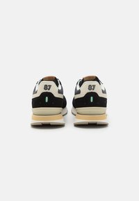 Black and cream sneakers featuring a suede and mesh upper, numbered 87 on the heel, with a textured midsole and rubber outsole.