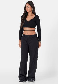 Zwarte geribbelde lange mouw crop top gecombineerd met zwarte cargobroek met zijzakken en een relaxte pasvorm. Casual schoeisel maakt de outfit compleet.