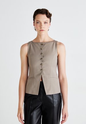 Beige sleeveless top with a round neckline, front buttons, two side pockets, and a tailored fit, paired with black leather pants.