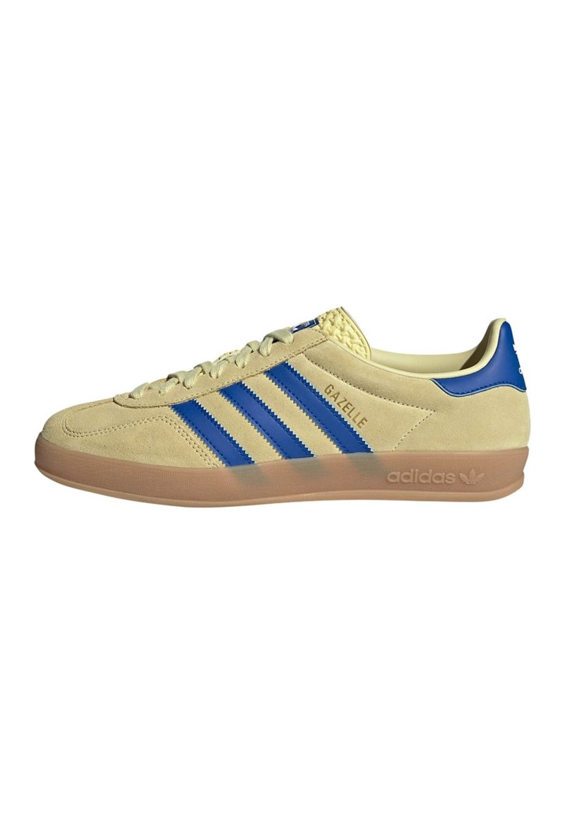 Tenisky Adidas Gazelle v béžové semišové kůži s modrými pruhy, gumovou podrážkou a texturovaným podpatkem. Šněrovací design s logovými akcenty.