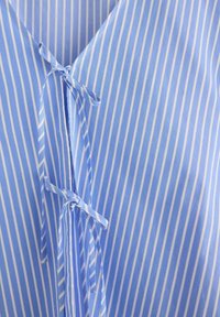 Blå og hvid stribet stof med lodrette linjer, med V-hals-design og en bindedetalje foran, lavet af letvægts bomuld.