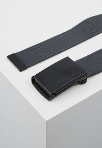 Black woven belt with a textured finish, rectangular metallic buckle featuring a gripping edge and engraved "URBAN CLASSICS."