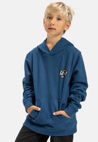Modrá mikina s kapucňou vyrobená z mäkkej tkaniny, s klokaním vreckom a logom na hrudi. Obsahuje kapucňu so sťahovacou šnúrkou a rebrované manžety.