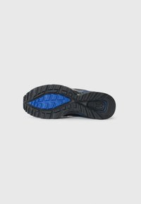 Semelle de sneaker noire et bleue arborant un motif en caoutchouc texturé, un relief prononcé pour l'adhérence, et un accent bleu moulé sur le bord extérieur.