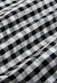 Tessuto a quadretti gingham bianco e nero con un motivo a scacchiera. La trama è tessuta, mostrando una combinazione di quadrati piccoli e grandi.