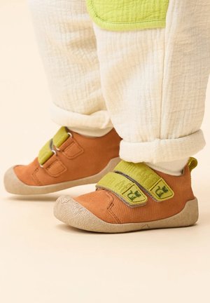 Oranje stoffen schoenen met groene klittenbandsluitingen, voorzien van een gestructureerde beige zool en een ronde neus. Draag met witte, gestructureerde broek.