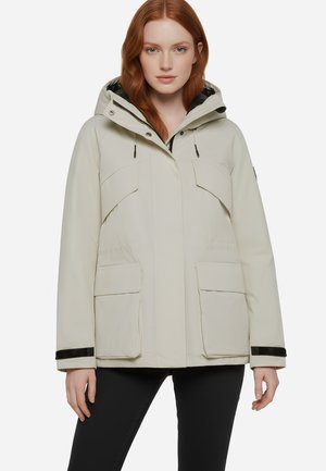 Giacca impermeabile beige con cappuccio, dotata di due tasche sul petto e due tasche laterali, dettagli neri sui polsini e una vestibilità morbida.