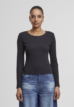 Črna dolga majica z izbočeno strukturo in okroglim izrezom, kombinirana s svetlo modrimi kavbojkami z bledenjem in sprednjimi žepi.