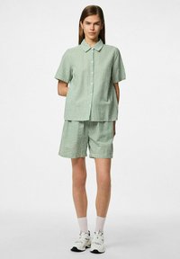 Groen-wit gestreept kortemouwen shirt, gecombineerd met bijpassende shorts in een zachte, gestructureerde stof. Het heeft een knoopsluiting aan de voorkant en een kraag.