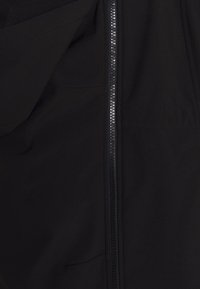 Czarna kurtka z częściowo otwartym suwakiem umieszczonym w centrum, odsłaniającym wewnętrzną tkaninę i szczegóły szycia.