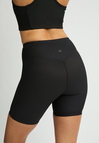 Pantaloni da ciclismo neri a coste con vita alta, caratterizzati da un leggero marchio sul retro e una texture liscia e elasticizzata per il massimo comfort.