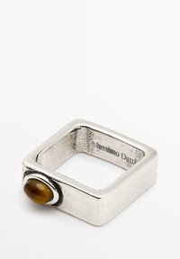 Quadratischer Silberring mit strukturiertem Finish, der an einer Seite einen glatten braunen ovalen Stein aufweist. Im Inneren eingravierter Markenname.