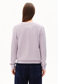 Licht lavendel gebreid truitje met ribbelstructuur, ronde hals en lange mouwen, gecombineerd met donkerblauwe corduroy broek met achterzakken.