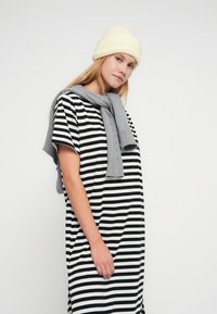 Μαύρο και άσπρο ριγέ φόρεμα τύπου t-shirt με κοντά μανίκια, συνδυασμένο με ανοιχτό γκρι πλεκτό κασκόλ και ανοιχτό κίτρινο σκουφάκι.