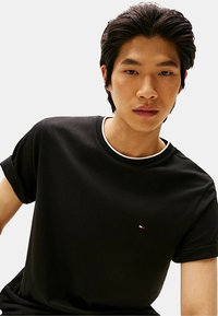 T-shirt in cotone nero con maniche corte arrotolate, caratterizzata da un piccolo logo ricamato in rosso, bianco e blu sul petto. Design classico con scollatura a girocollo.