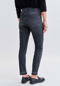 Jeans in denim nero con una vestibilità slim, dotati di tasche posteriori, orlo sfrangiato e una texture liscia. Indossati con scarpe nere senza lacci.