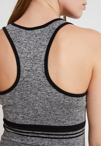 Grå, texturerad sporttopp med racerback-design och svart kant, med en horisontell randaccent på den nedre bandet.