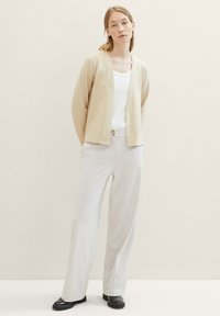 Beige cardigan med en texturerad yta, vit linne under, och ljusgrå vida byxor. Svarta loafers fulländar looken.