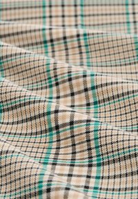 Beige plaid fabric featuring black and teal checks, with a textured weave, creating a subtle visual depth. Soft and drapes gently.