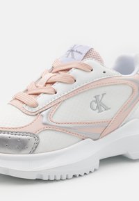 Weiße Sportsneaker mit rosa Akzenten, silbernen Details, luftdurchlässiger Zunge und strukturiertem Stoff. CK-Logo an der Seite sichtbar.